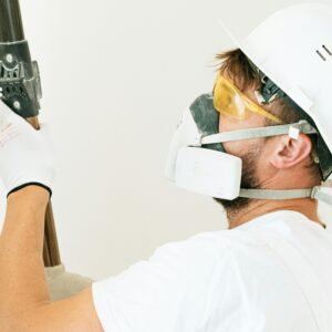 Construction worker wearing safety gear applying paint with a roller indoors. Focus on safety measures.