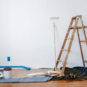 A room prepared for renovation with a ladder, paint supplies, and drop cloth.